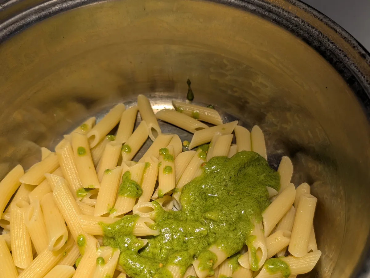 Penne cuits dans le chaudron avec le pesto de feuilles de zucchini déposé dessus, avant de mélanger