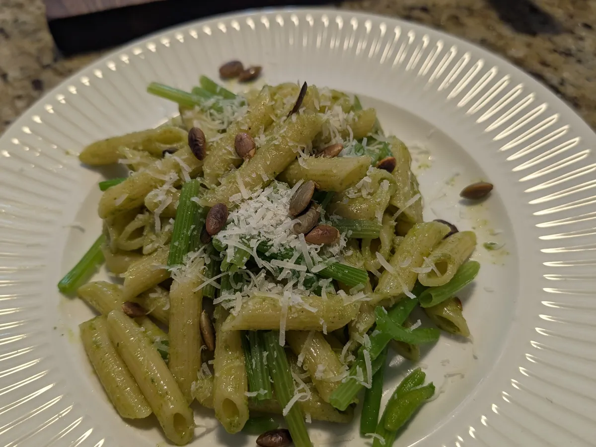 Vue du dessus d'une assiette de penne au pesto de feuilles de zucchini, garnie de pecorino râpé et de graines de citrouille grillées