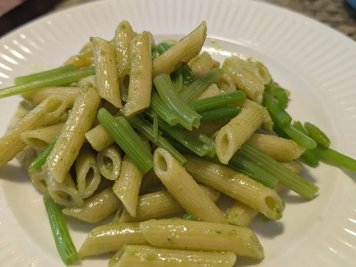 Assiette de penne au pesto de feuilles de zucchini avec de nombreux tronçons de tiges de zucchini vert vif